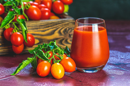 Glass of fresh delicious jummy red tomato juice and fresh tomatoes in wooden box. Dark background. Close up. Gmo free. Natural good food