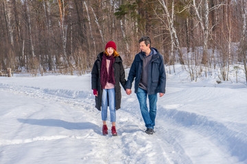 Fototapeta na wymiar Handsome man and attractive young woman walking along snowy country road in sunny day. Beautiful look, male and female fashion, winter outfit. Winter holidays, weekend at countryside concept