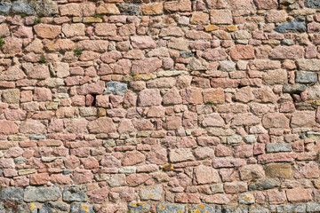 Fragment of the fortress wall of pink stones. Stones of various shapes are carefully adjusted to each other. Semur-en-Osua. Burgundy. France. Texture. Background.
