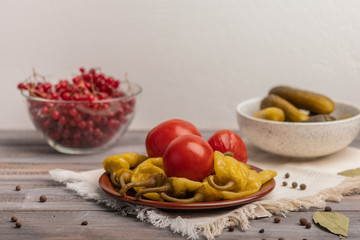 Homemade pickled peppers and tomatoes on a ceramic plate on a linen napkin. Near pickles and viburnum in bowls