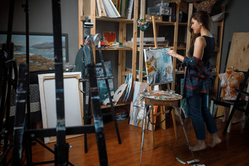 Pretty Girl artist paints on canvas painting on easel in workshop