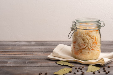 Homemade canned cabbage in jar on napkin with bay leaves on a wooden table. Rustic style