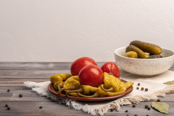 Homemade pickled peppers and tomatoes on a ceramic plate on a linen napkin. Near pickles in a salad bowl