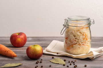 Homemade canned cabbage in jar on napkin with apple on a wooden table. Rustic style