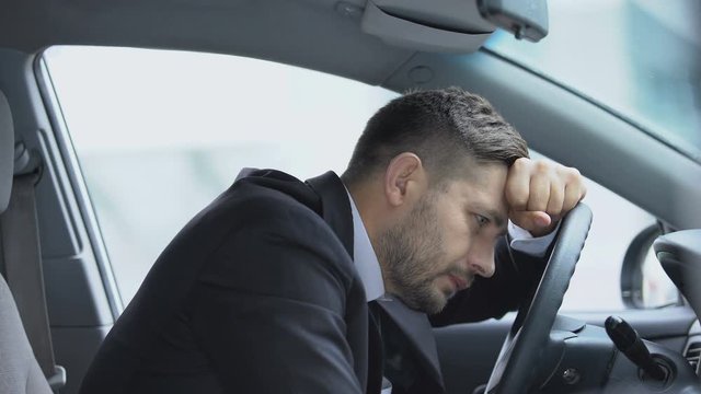 Exhausted driver leaning on steering wheel to relax, stressful job, overworking