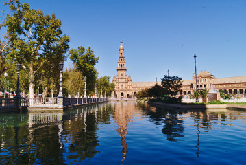 Fototapeta na wymiar Views of the Seville Plaza de Espana from the side, where the main tower is reflected in the water of the canal on a sunny day