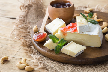Brie type of cheese with jam. Camembert cheese. Fresh Brie cheese and a slice on a wooden board with nuts, honey and leaves. Italian, French cheese.