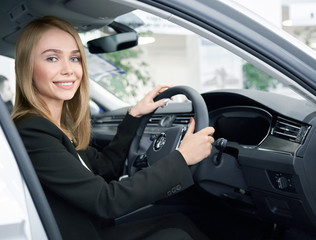 Young woman sitting in right handed automobile in auto salon