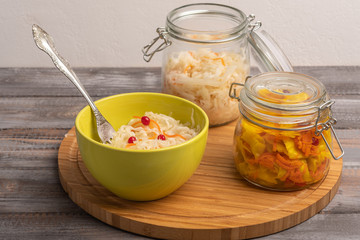 Homemade sauerkraut in two jars with a salad bowl and a fork on a wooden board. Rustic style