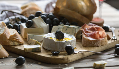 Assorted cheeses on wooden board. Camembert, cheese with blue mildew, gouda, hard cheese, strawberries, mint leaves, knives for cheese.