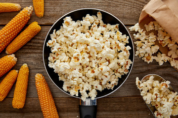 top view of popcorn in frying pan near ripe corn on wooden background