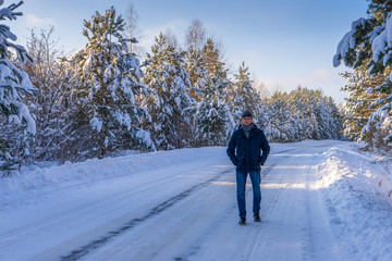 Handsome middle-aged man against beautiful winter snowy landscape. Man walking along forest road in sunny frosty day. Human and nature, winter holidays, weekend at countryside concept