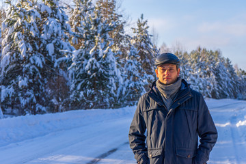 Fototapeta na wymiar Portrait of handsome middle-aged man against beautiful winter landscape. Man walking along forest road in sunny frosty day. Human and nature, winter holidays, weekend at countryside concept