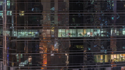 Office skyscraper exterior during late evening with interior lights on and people working inside night timelapse