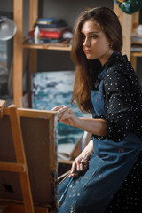 Portrait talented artist girl in workshop is working at easel with new painting
