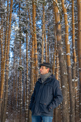Portrait of handsome middle-aged man against beautiful winter landscape. Man walking in snowy forest in sunny frosty day. Human and nature, winter holidays, weekend at countryside concept