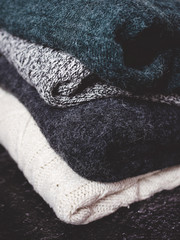 Pile of chunky winter sweaters laying on dark textured desk or table.
