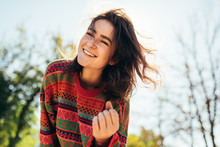 Bottom view portrait of happy beautiful young woman smiling broadly with windy hair and freckles enjoying the warm autumn weather, wearing sweater, posing on nature sunlight background.