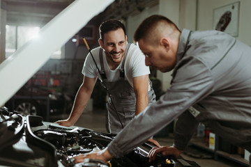 Fototapeta na wymiar Auto mechanics talking while analyzing a car engine in a workshop