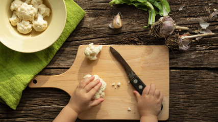 Cooking Cauliflower. Top view, wooden table. The child helps to cook