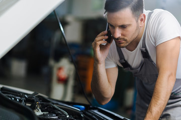 Auto mechanic talking on mobile phone in auto repair shop - Powered by Adobe