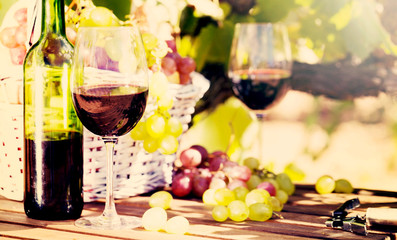 still life with glass of red wine grapes and picnic basket on table