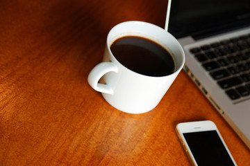 Hot Americano in white cup with laptop and smartphone on wooden table in cafe. Hot drink have computer notebook and mobile phone background on desk at workplace.