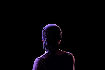 Fototapeta premium Silhouette of a guy in a dark T-shirt and bandana in back modeling light on a black background. View of a man from the back. Isolated. Copy space.