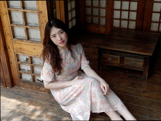 Beautiful young woman sitting on Japanese style floor barefoot, leaning against wooden and paper door, looking smiling at camera with lonely expression, portrait of Chinese beautiful girl in summer.