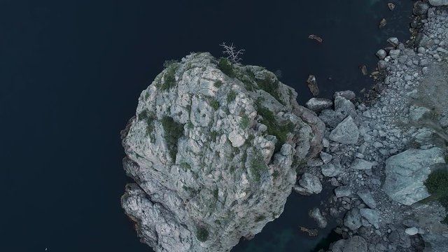 Magnificent sea with dark blue water and impregnable rocks covered with green trees and bushes. Shot. Top view of steep cliff and the sea coast with small soft ripples.