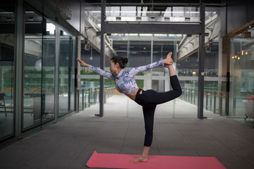 Fototapeta premium Young attractive smiling woman practicing yoga, sitting in One Legged King Pigeon exercise, Eka Pada Rajakapotasana pose, working out, wearing sportswear, grey pants, bra, indoor full length, home