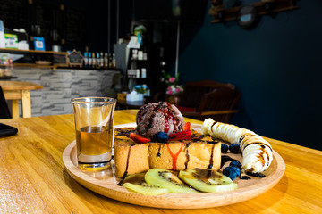 Chocolate ice cream is placed on a toast on a wooden tray, served with bananas, kiwi and honey on the coffee table.