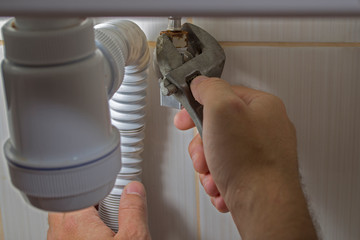 A man repairs plumbing under the sink with his right hand unscrews the nut fixing the flexible...