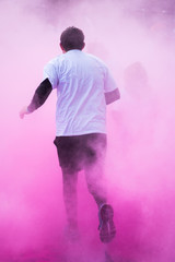Des personnes courent dans une fumée colorée rose holi. Un coureur dans de la fumée rose. Un...