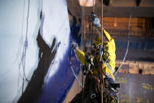 Picture of secondary safety back up device with blurry of rope access industry worker wearing safety harness, abseiling respirators for spray painting protection construction site Perth, Australia 