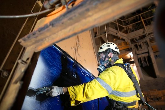Close up picture of rope access technician wearing fully safety harness equipment a chemical respirators for spray painting protection spray mask protection descending abseiling commencing spraying 
