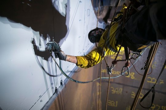 Close up picture of rope access painter working at height abseiling upside down wearing safety chemical protective mask  commencing spray painting in confined space construction site Perth, Australia