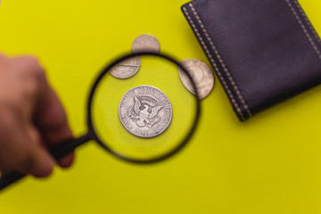 Black leather Men's Wallet with American coins under a magnifying glass on yellow background.