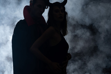 silhouette of man and woman in halloween costumes standing on black with smoke