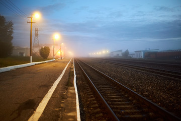 Fototapeta na wymiar night railway is lit by yellow lanterns in the fog