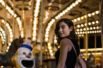 Young woman in a fair, carousel lights in the background
