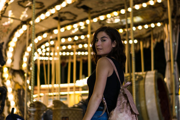 Young woman in a fair, carousel lights in the background
