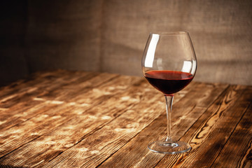 A glass of red wine on a wooden table in the cellar of the winery. Place for text or advertising