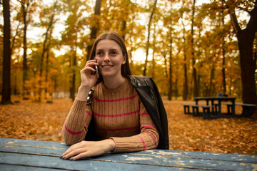  Beautiful girl emotionally speaks on the phone in the autumn park. Colorful autumn. Lifestyle.