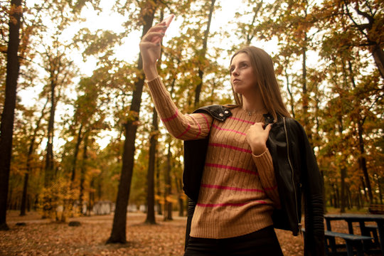    Beautiful girl takes pictures on the phone in the autumn park. Selfie. Wonder autumn. Lifestyle.