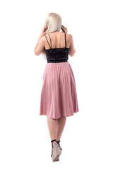 Back view of classy blonde woman in elegant clothes talking on the phone walking away. Full body isolated on white background. 