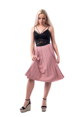 Elegant feminine blonde woman in evening wear lifting skirt looking down at feet. Full body isolated on white background. 