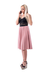 Worried displeased young well dressed woman in skirt looking down and talking on the cellphone. Full body isolated on white background. 