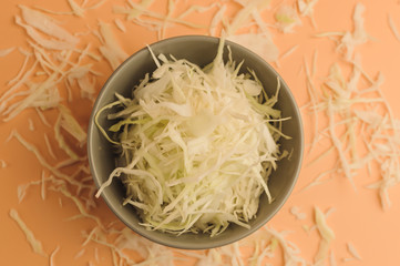 Finely chopped white cabbage on beige background,cabbage in bowl and around on the surface,chopped cabbage in minimalist style,rustic vegetables, vegetarian product, vitamins, healthy eating concept.