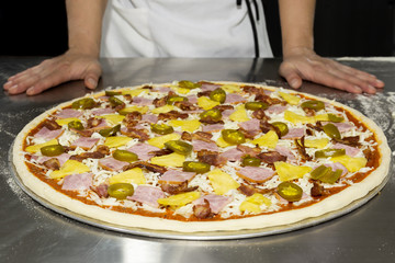 Chefs hand with hawaiian pizza and pineapple, pickled chilli ,ham on the table.